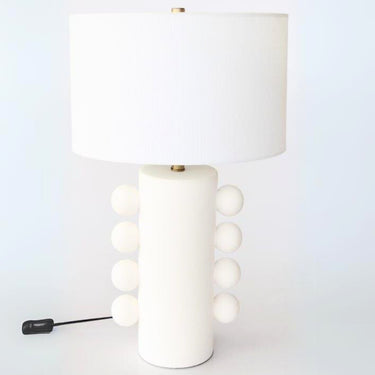 Side bobble ceramic table lamp with white textured ceramic base showing four circular bobbles on each side and brass neck finish