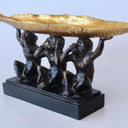 side view of gold bowl and black monkey figures on neutral background