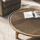 Sandpiper wood coffee table with a mango wood round top in a vintage finish styled in modern living room with chair and beige rug.