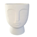 A white concrete face planter with a stylized human face design, suitable for housing plants.