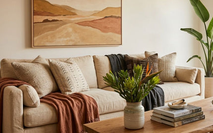 Earthy living room interior featuring a beige linen sofa, rustic wooden coffee table with a green plant, large abstract landscape art, and a bird of paradise potted plant