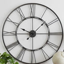 Large open-frame skeleton metal wall clock hung as a functional art centerpiece on a neutral living room wall.