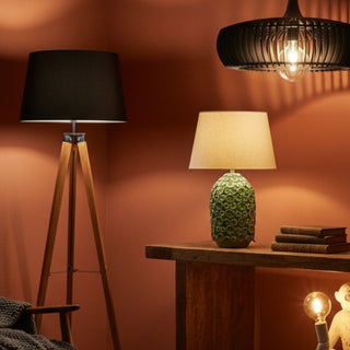 Modern lighting collection featuring a wood tripod floor lamp, a black slatted pendant light, a green textured ceramic lamp, and a white monkey lamp tucked under a rustic console