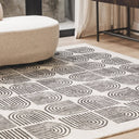 lounge living space styled with a large Arcade charcoal and natural cream geometric wool rug next to a contemporary curved sofa.