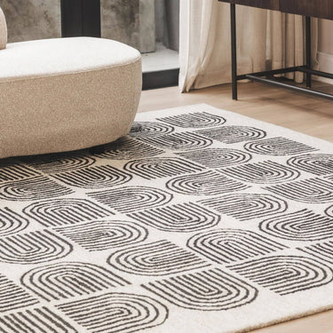 lounge living space styled with a large Arcade charcoal and natural cream geometric wool rug next to a contemporary curved sofa.