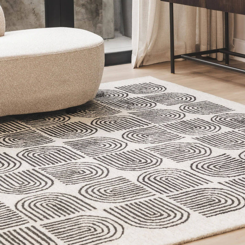 lounge living space styled with a large Arcade charcoal and natural cream geometric wool rug next to a contemporary curved sofa.