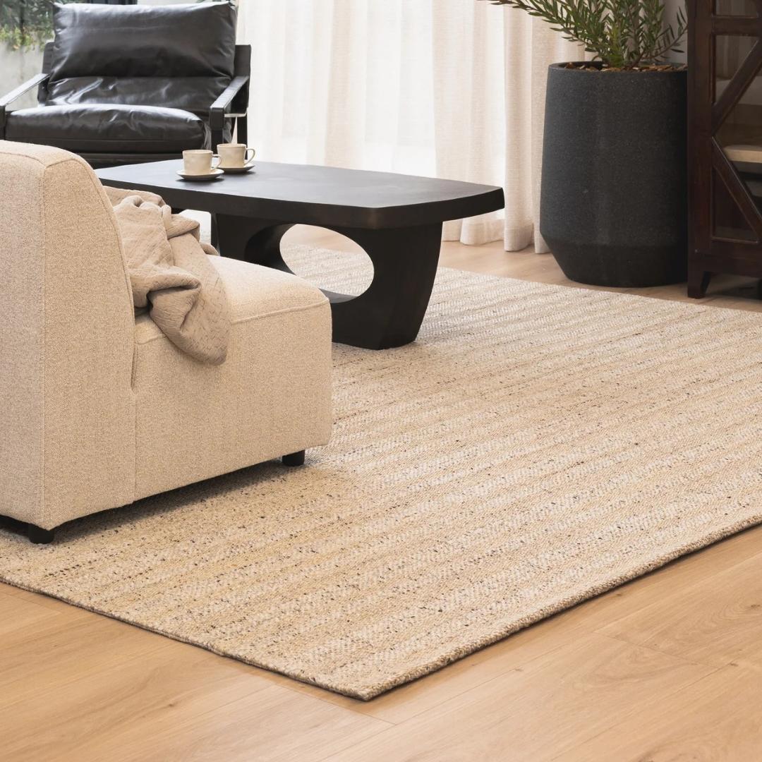 Handloom-crafted, wool-rich rug with a subtle stripe layer under a dark wood coffee table in a living room.