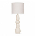 A modern table lamp with a textured off-white fabric drum shade and a sculptural, stacked ceramic base in a matching cream colour.
