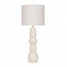 A modern table lamp with a textured off-white fabric drum shade and a sculptural, stacked ceramic base in a matching cream colour.