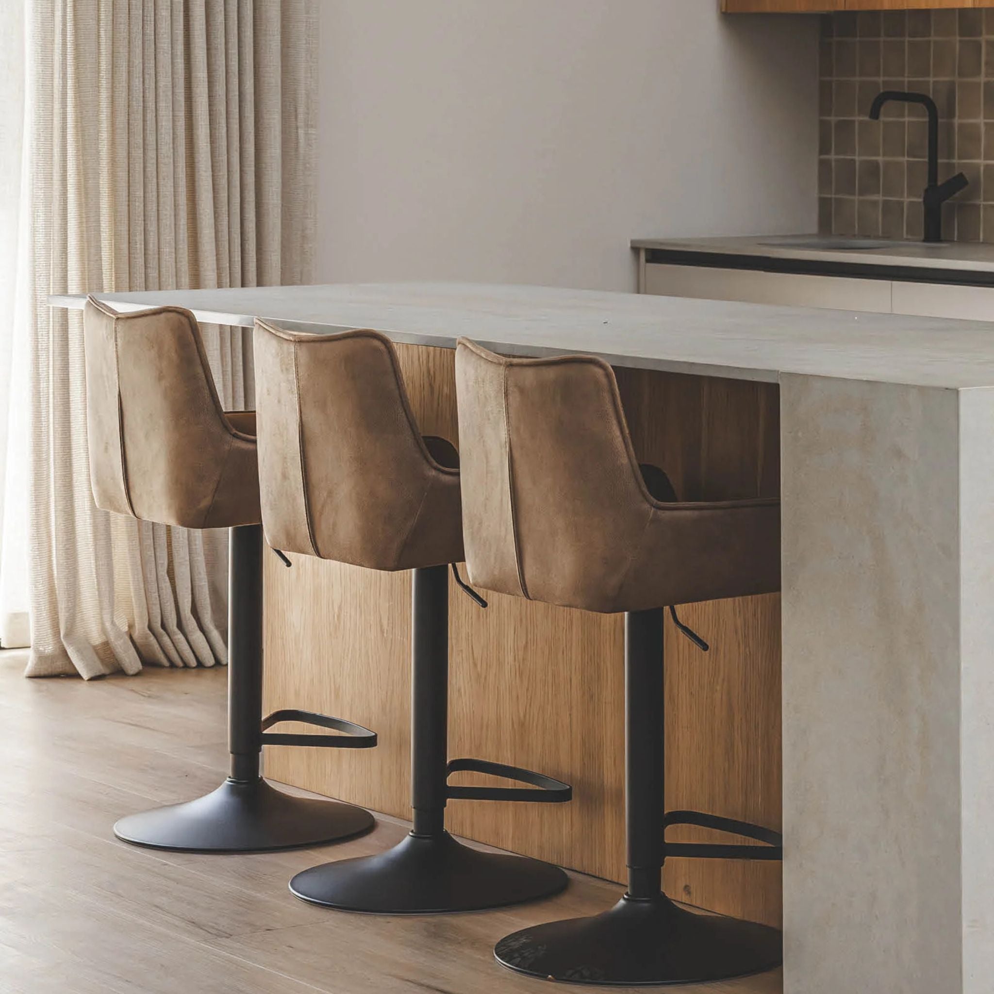 Three brown bar stools with black bases in front of a kitchen counter.