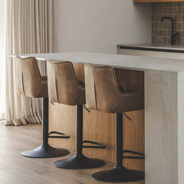 Three brown bar stools with black bases in front of a kitchen counter.