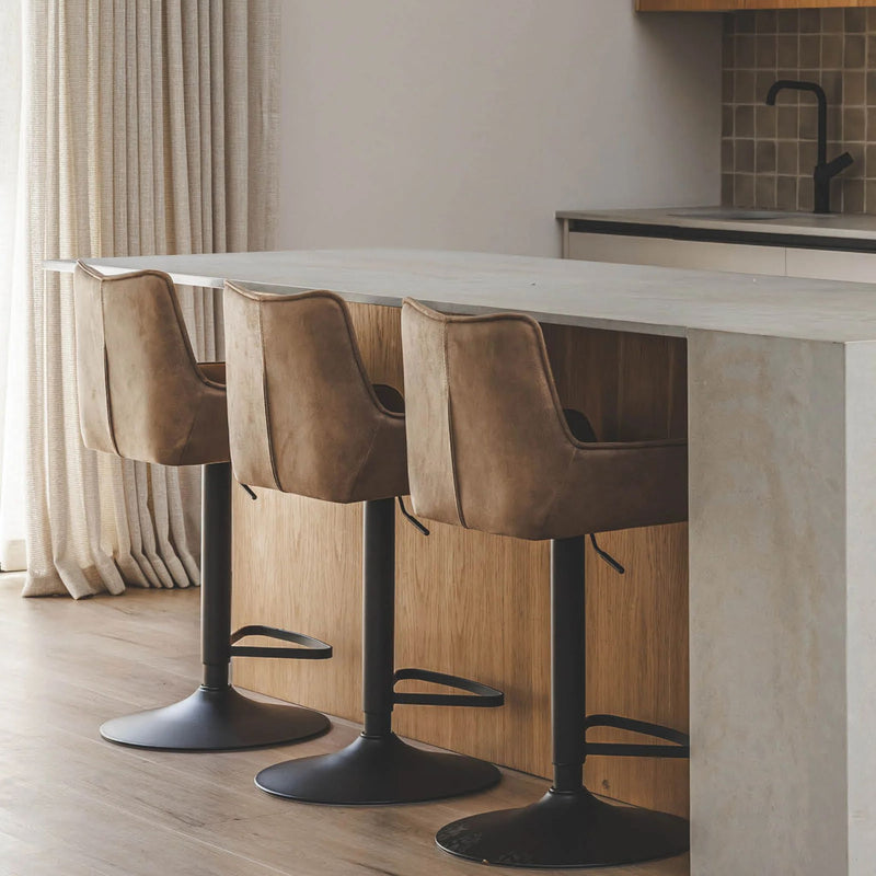 Three brown bar stools with black bases in front of a kitchen counter.