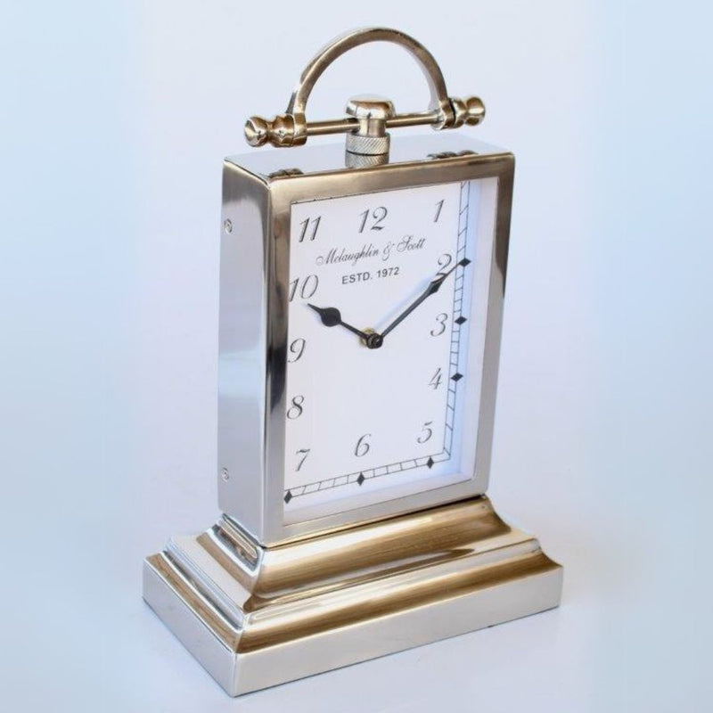 Polished nickel tabletop analog clock with italic script numbers, spade hands, and a top handle.