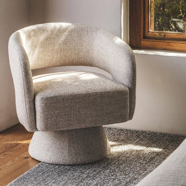 A modern barrel-style swivel armchair upholstered in textured light beige fabric, in a bedroom.