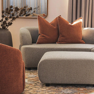 Echo Ottoman in Hertex Pascal Linseed placed on a rug next to a couch in a modern living room setting