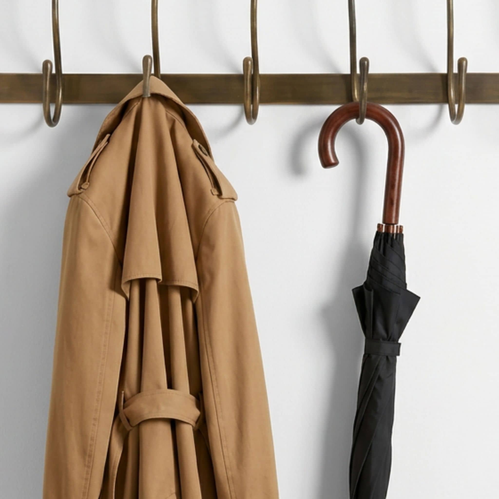 Hang-Out wall hooks by Woodka Interiors in a hand-finished antique brass, styled with a coat and umbrella hanging in entryway.