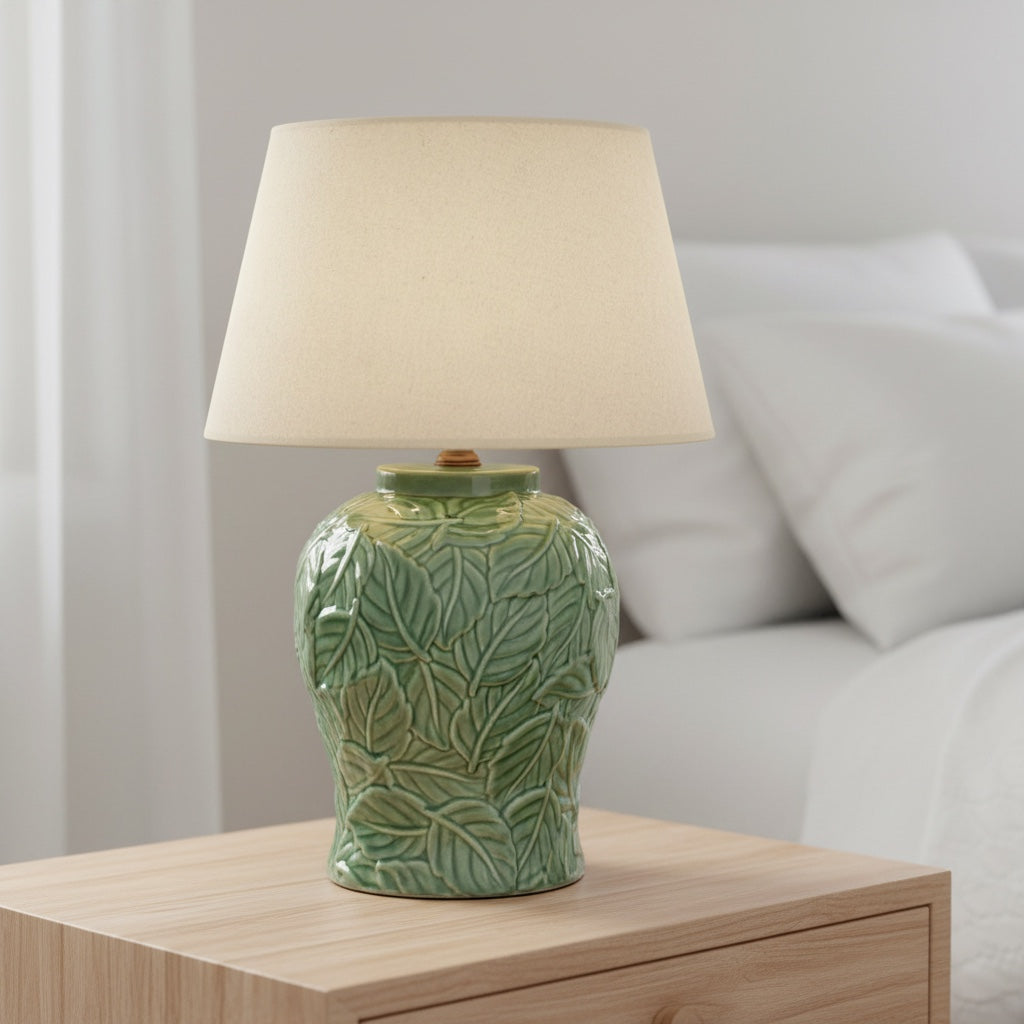 Green ceramic lamp with beige shade on a wooden bed side table 