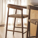 Two solid teak and handwoven rope counter chairs positioned next to a light oak wood kitchen island.