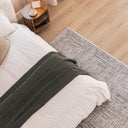 Dark toned area rug with concentric pattern under a bed in a modern bedroom setting.