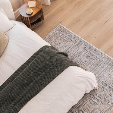 Dark toned area rug with concentric pattern under a bed in a modern bedroom setting.
