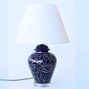 navy blue table lamp features swirling pattern of blue and black on a ceramic base that sits on a clear glass pedestal. 