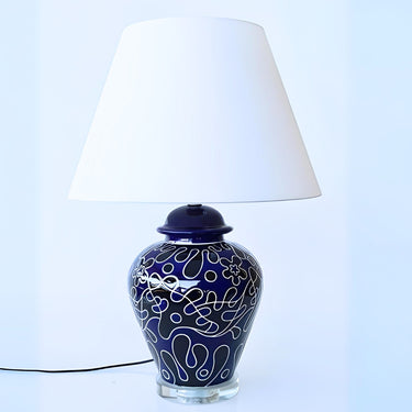 navy blue table lamp features swirling pattern of blue and black on a ceramic base that sits on a clear glass pedestal. 