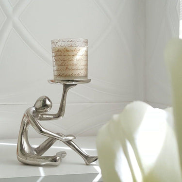 Modern decorative candle holder with minimalist seated figure in silver finish with a scented canlde on a table top