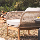 Vision Outdoor Teak Occasional Chair with rope detailing and teak frame on a pebbled surface with greenery in the background