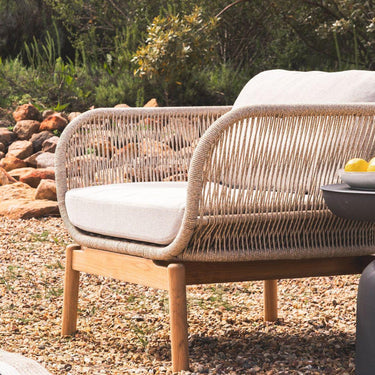 Vision Outdoor Teak Occasional Chair with rope detailing and teak frame on a pebbled surface with greenery in the background