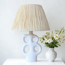 White ceramic table lamp with cut-out base and raffia lampshade on console table