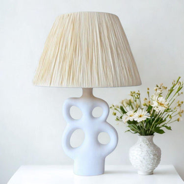 White ceramic table lamp with cut-out base and raffia lampshade on console table