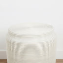 White rattan stool side table on a wood floor in a neutral room
