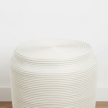 White rattan stool side table on a wood floor in a neutral room