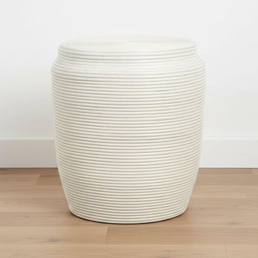 White rattan stool side table on a wood floor in a neutral room