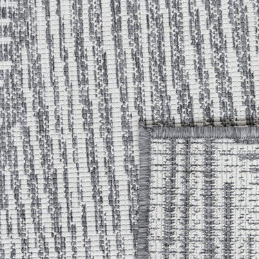 close up of reversible fully outdoor area rug in geometric pattern of triangles and lines in grey and off-white design.