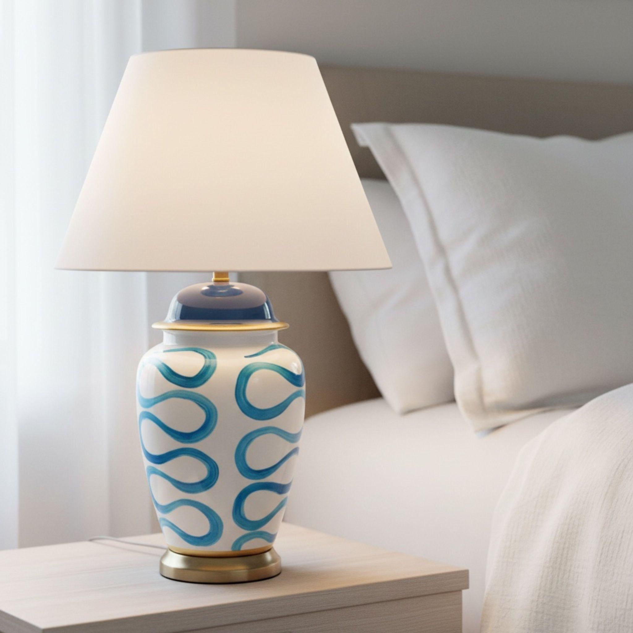 The Blue Swirl Lamp providing a warm soft glow on a bedside table in a coastal-inspired bedroom setting.