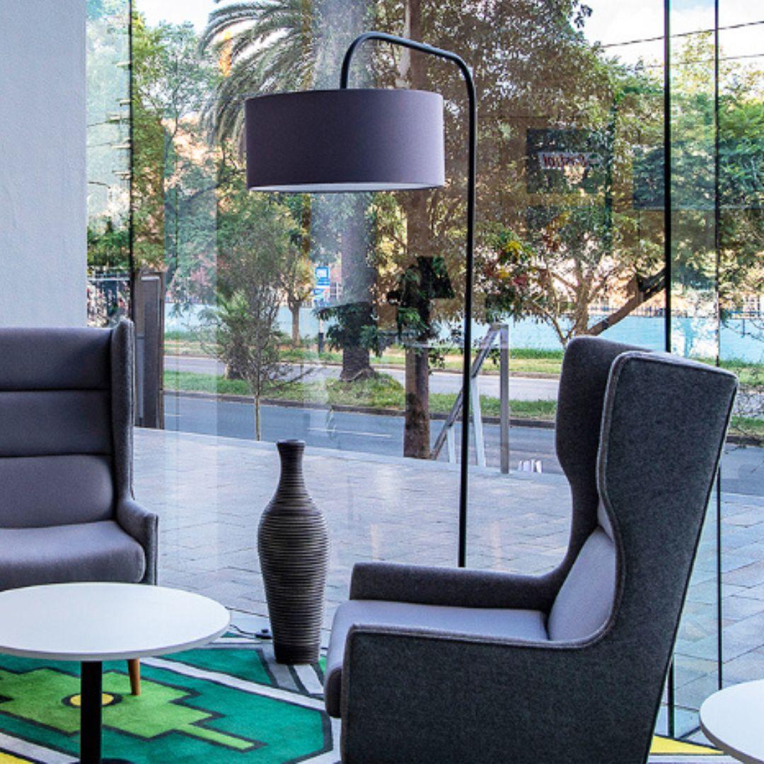 Modern interior with gray armchair, round table, and decorative vase in front of large glass windows featuring a Standing lamp with black drum shade