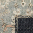 Close-up of a distressed area rug showing its faded beige and blue pattern, and a dark charcoal woven backing.