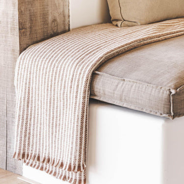 celine striped throw blanket is draped over  a cushioned bench