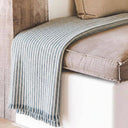 Celine striped throw blanket with fringe is draped over a beige bench indoor setting.