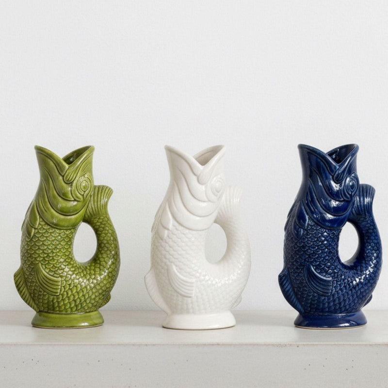 Three sculpted koi fish jug vases lined up in olive green, white, and deep navy ceramic