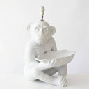 A glossy white ceramic table lamp shaped like a seated monkey holding a leaf, with a visible light socket at the top, photographed against a plain white background.