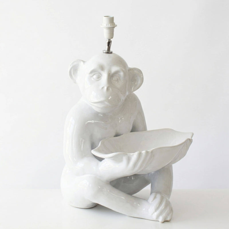 A glossy white ceramic table lamp shaped like a seated monkey holding a leaf, with a visible light socket at the top, photographed against a plain white background.