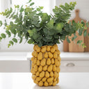 Modern yellow ceramic vase filled with fresh eucalyptus stems styled as a colorful focal point on a kitchen counter.