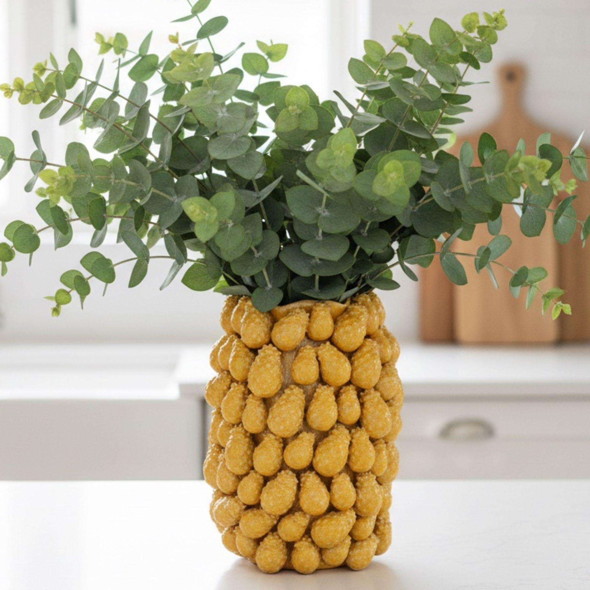 Modern yellow ceramic vase filled with fresh eucalyptus stems styled as a colorful focal point on a kitchen counter.