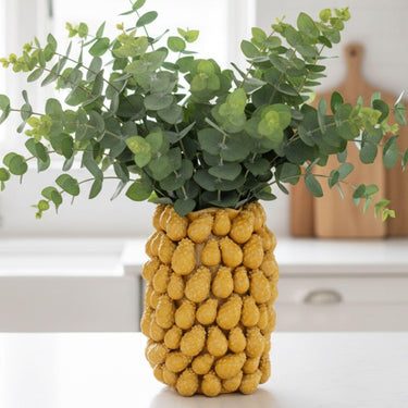 Modern yellow ceramic vase filled with fresh eucalyptus stems styled as a colorful focal point on a kitchen counter.