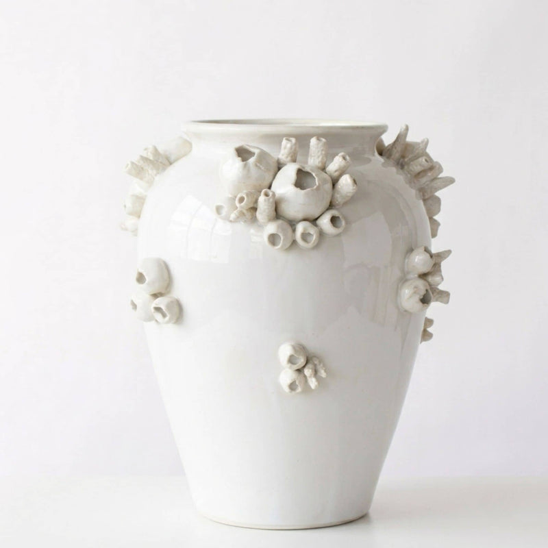 A glossy white ceramic vase decorated with raised, organic coral-like sculptural details in off-white and light gray, photographed against a clean white studio background.