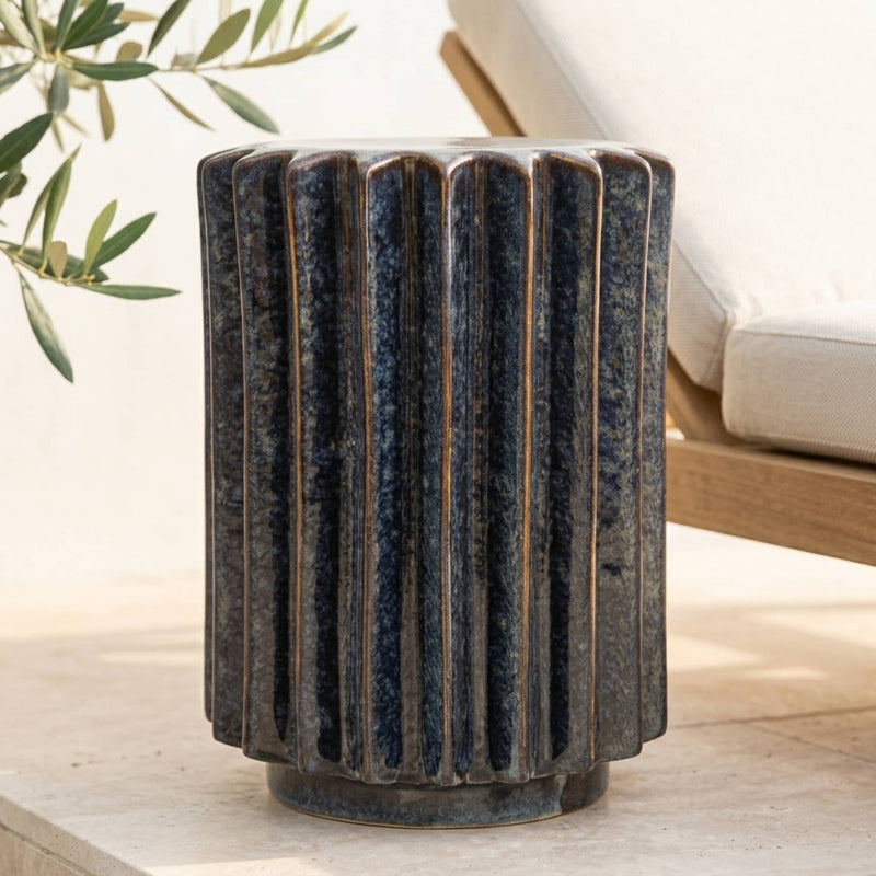 A dark blue-gray fluted side table or with a textured smooth glaze, shown in an outdoor patio setting.