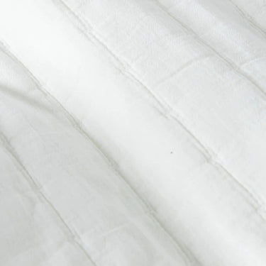 A close-up of white quilt bedspread with a stitched diagonal paneling.