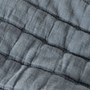 A close-up of a quilted fabric with a textured, crinkled linen-like surface in a muted slate blue colour.